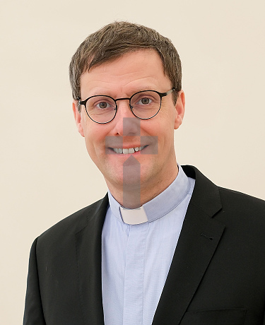 Porträtfoto von Weihbischof Dr. Martin Marahrens, im schwarzen Anzug mit blauem Hemd und Priesterkragen, freundlich lächelnd